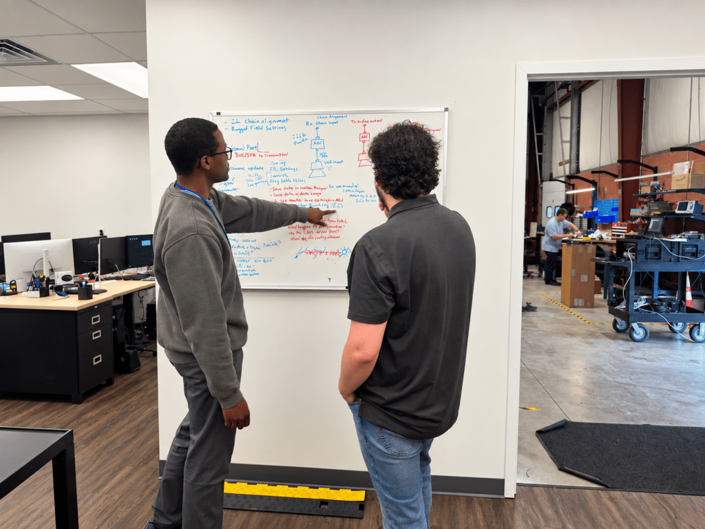 Kyle collaborating with a fellow Lite Coms engineer while reviewing technical diagrams on a whiteboard.