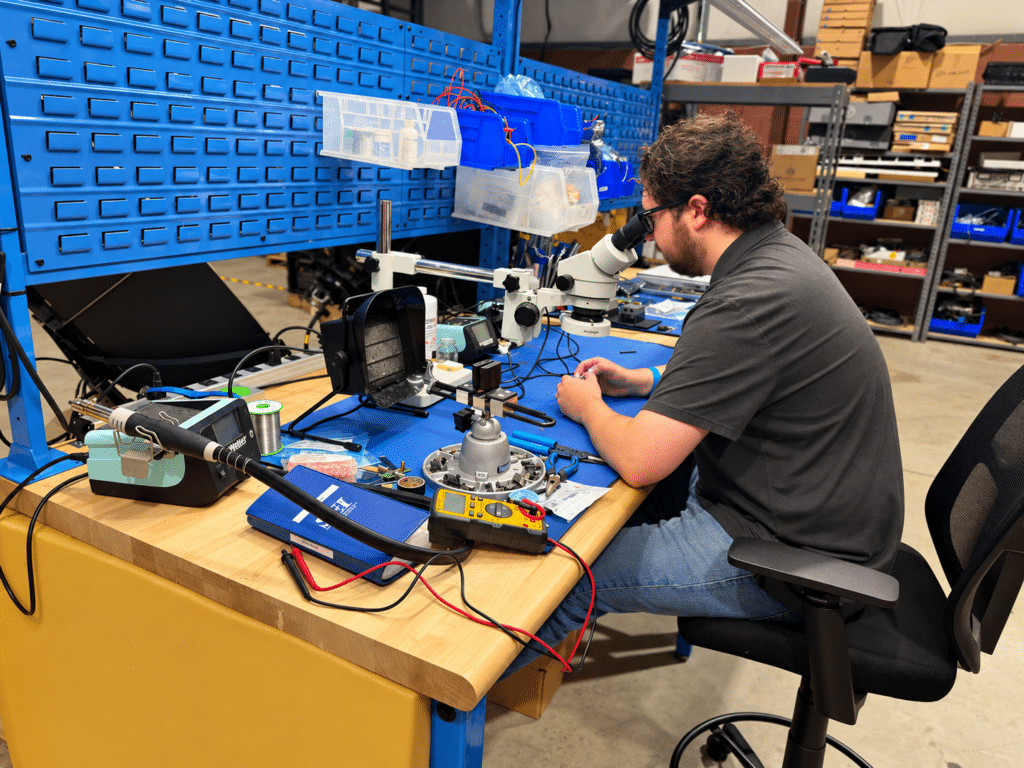 Lite Coms electrical engineer Kyle working hands-on with electronic components under a microscope.